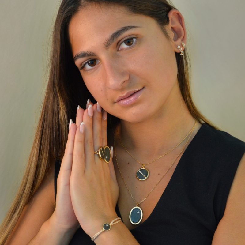 Collier plaquée or avec pendentif rond intérieur en pyrite (noire) avec un trait esthétique brillant dans son diamètre. Bijou porté, Crédit GEMITY.