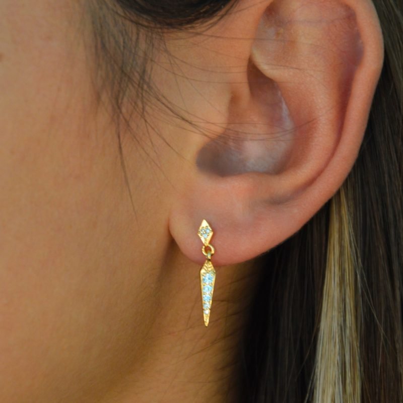 Boucle d'oreille plaquée or pendante. L'accrochet est un losange recouvert de brillants et la partie pendante est un losange alongé vers le bas comportant elle aussi des brillants. Bijou porté, Crédit GEMITY.