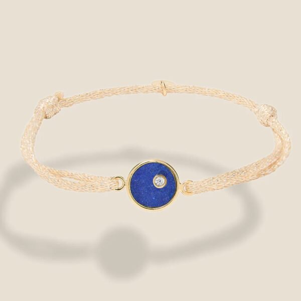 Bracelet ajustable, cordon beige pailleté, plaque ronde en plaqué or intérieur Lapis lazuli. Bijou seul, Crédit Léo Sédim.