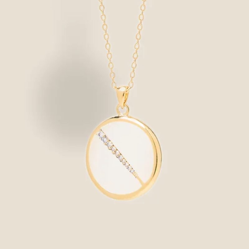 Collier plaquée or avec pendentif rond intérieur en nacre (blanc) avec un trait esthétique brillant dans son diamètre. Bijou seul, Crédit Léo Sédim