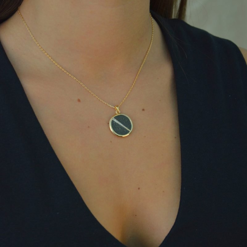Collier plaquée or avec pendentif rond intérieur en pyrite (noire) avec un trait esthétique brillant dans son diamètre. Bijou porté, Crédit GEMITY.