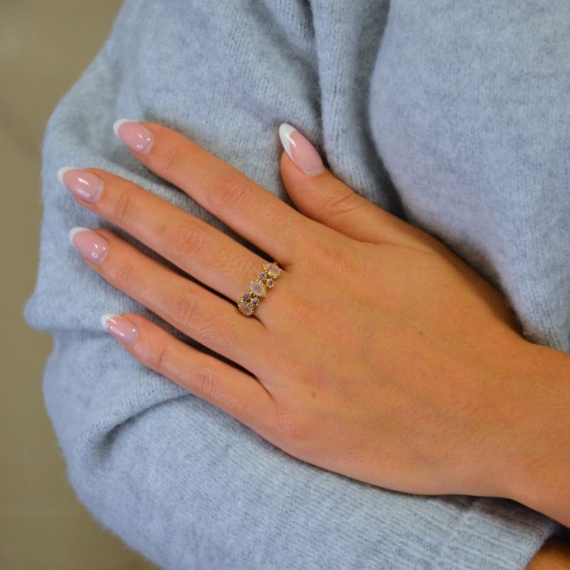 Notre bague Ondine en plaqué or est un bijou qui allie glamour et raffinement, ornée d'une succession de pierres semi-précieuses en quartz rose, améthyste, labradorite et zircon.. Bijou porté, Crédit GEMITY.
