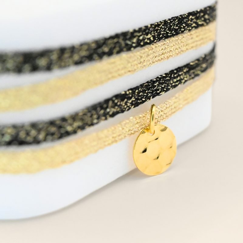 "Bracelet double tours en tissu de deux coloris différents avec une pastille martelée dorée à l’or fin. Fermoir en plaqué or réglable . Bijou seul, Crédit GEMITY"