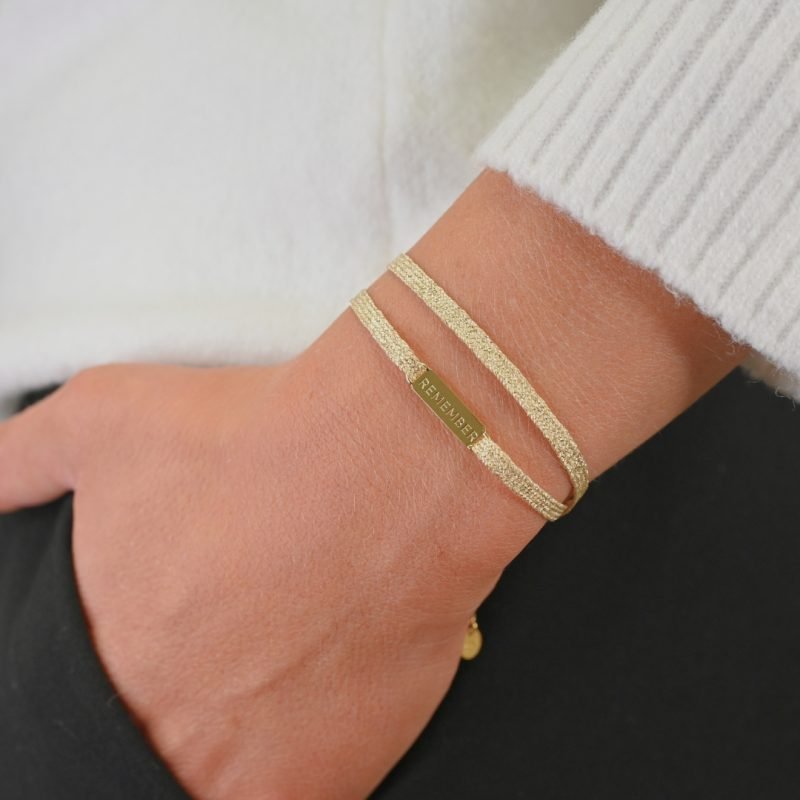 "Bracelet double tours en tissu avec une plaque REMEMBER en plaqué or (3 microns) fait main. Fermoir en plaqué or réglable . Bijou porté, Crédit GEMITY."