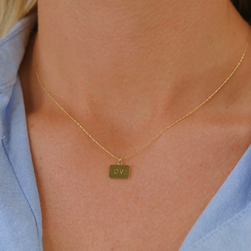 Collier plaqué or avec plaque extra-fine réversible, inscription LOVE d'un côté et émail noir pailleté de l'autre côté. Bijou porté, Crédit GEMITY.