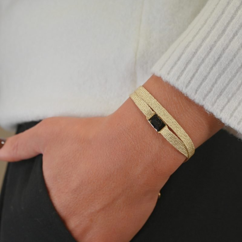 "Bracelet double tours en tissu avec une plaque noire pailleté en plaqué or (3 microns) fait main. Fermoir en plaqué or réglable . Bijou porté, Crédit GEMITY."