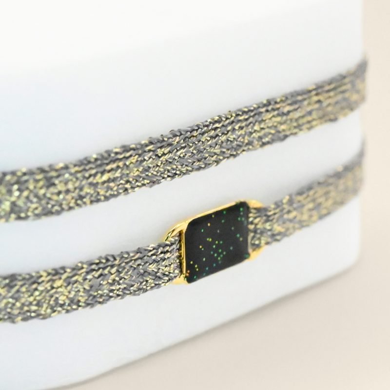 "Bracelet double tours en tissu avec une plaque noire pailleté en plaqué or (3 microns) fait main. Fermoir en plaqué or réglable . Bijou porté, Crédit GEMITY."