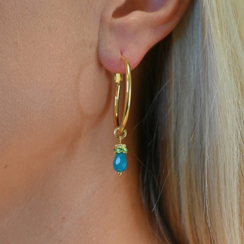 Découvrez l’élégance intemporelle de cette créole doré à l’or fin, ornée d’un délicat pendentif en pierre de jade teinté. Ces boucles d’oreilles allient sophistication et modernité, parfaites pour sublimer toutes vos tenues, qu’elles soient décontractées ou habillées. Bijou porté, Crédit GEMITY.