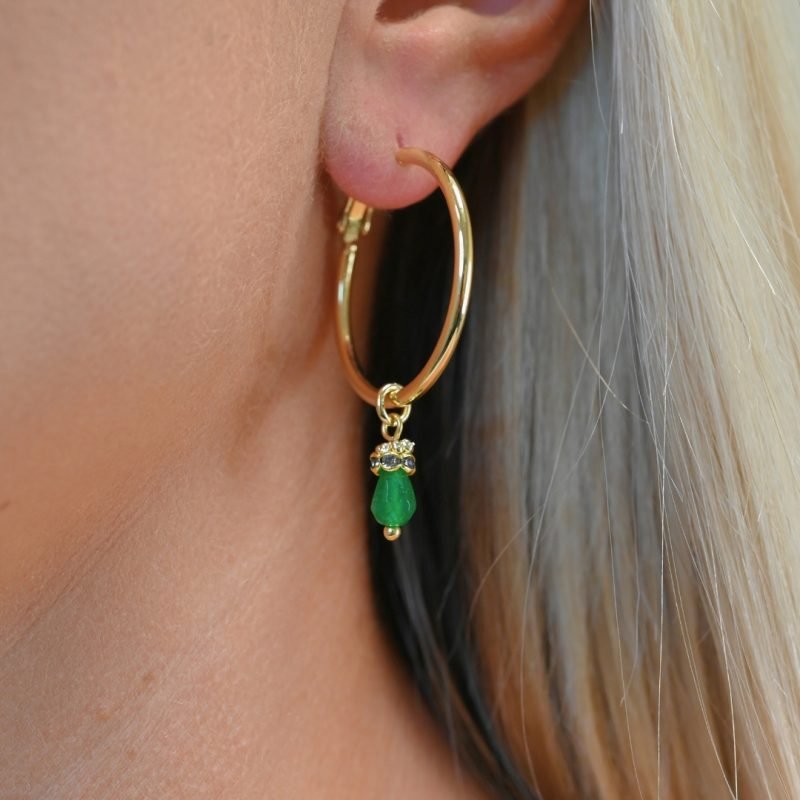 Découvrez l’élégance intemporelle de cette créole doré à l’or fin, ornée d’un délicat pendentif en pierre de jade teinté. Ces boucles d’oreilles allient sophistication et modernité, parfaites pour sublimer toutes vos tenues, qu’elles soient décontractées ou habillées. Bijou porté, Crédit GEMITY.