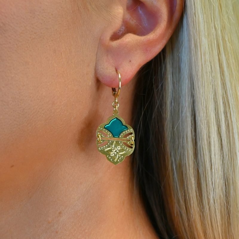 Comme un hommage aux volutes de l'architecture et palais indiens, ces boucles d’oreilles tout en courbes sublimeront votre visage. Elles sont émaillées de résine colorée transparente qui donne de la profondeur à la boucle. Elles sont en 2 parties pour plus de fluidité et de légèreté. La partie inférieure est gravée d'une fleur à 4 pétales. D'un style bohème chic, ce joli modèle vous accompagnera partout. Bijou porté, Crédit GEMITY.