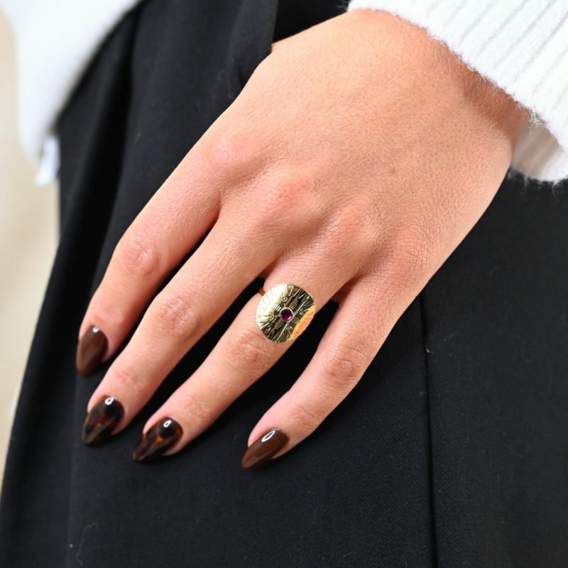Cette jolie bague habille votre doigt avec son motif rond et courbé. Elle est gravée de motifs et surmonté d'un cabochon de couleur, émaillé à la main. Bijou porté, Crédit GEMITY.
