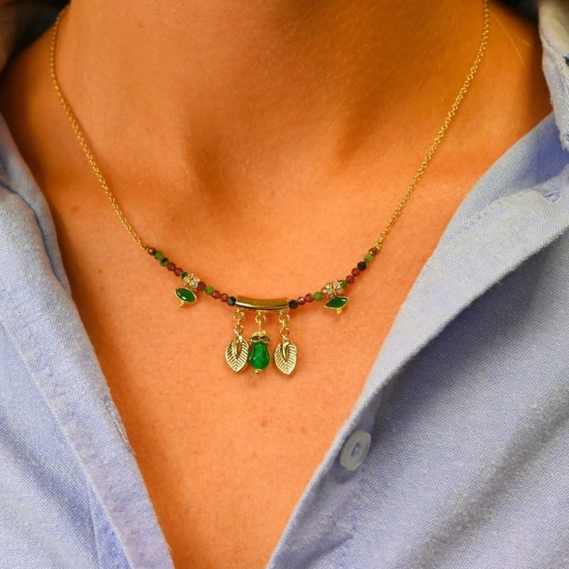 "Les pampilles feuilles rappellent l'univers luxuriant des motifs indiens, les rondelles de strass soulignent les pierres serties et les fines perles donnent du cachet à ce collier bohème! laiton doré à l’or fin 24 carats, cordon polyester et coton. Pierres serties (agate verte et tourmaline rose), jade teinté, perles en pierre semi-précieuses, strass . Bijou porté, Crédit GEMITY."
