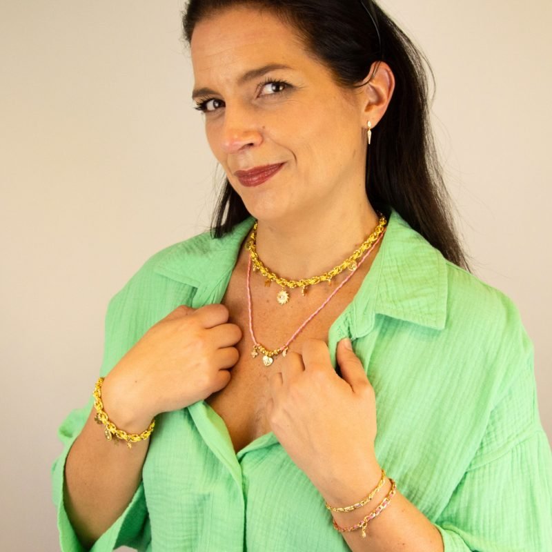 "Bracelet avec un cordon doré et un gemme transparent en son centre. Composition : 100% plaqué or. Contient 1 strass coloré transparent. . Bijou porté, Crédit GEMITY."