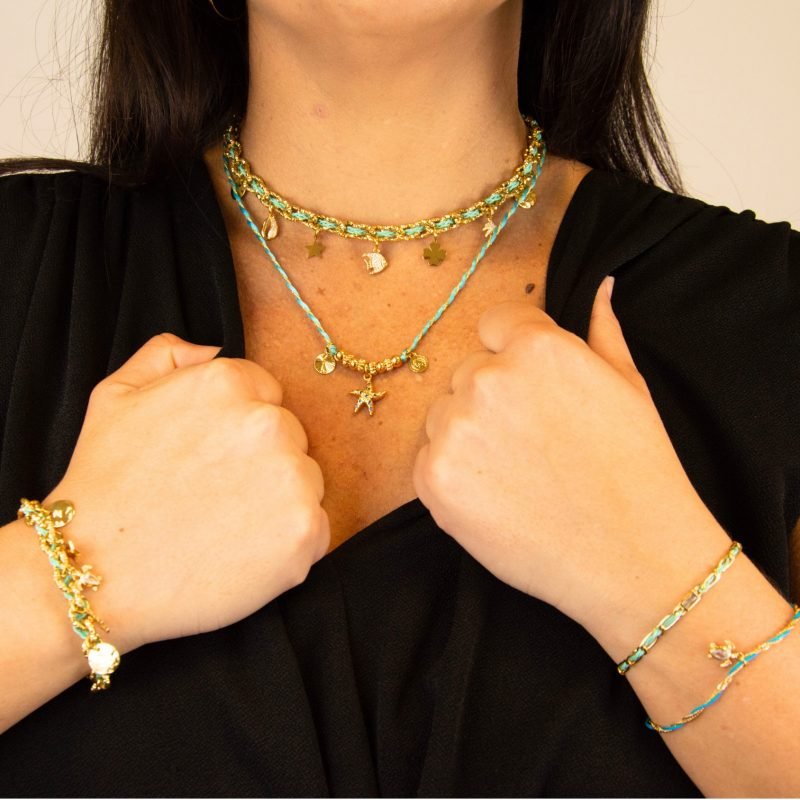"Bracelet avec un cordon doré et un gemme transparent en son centre. Composition : 100% plaqué or. Contient 1 strass coloré transparent. . Bijou porté, Crédit GEMITY."