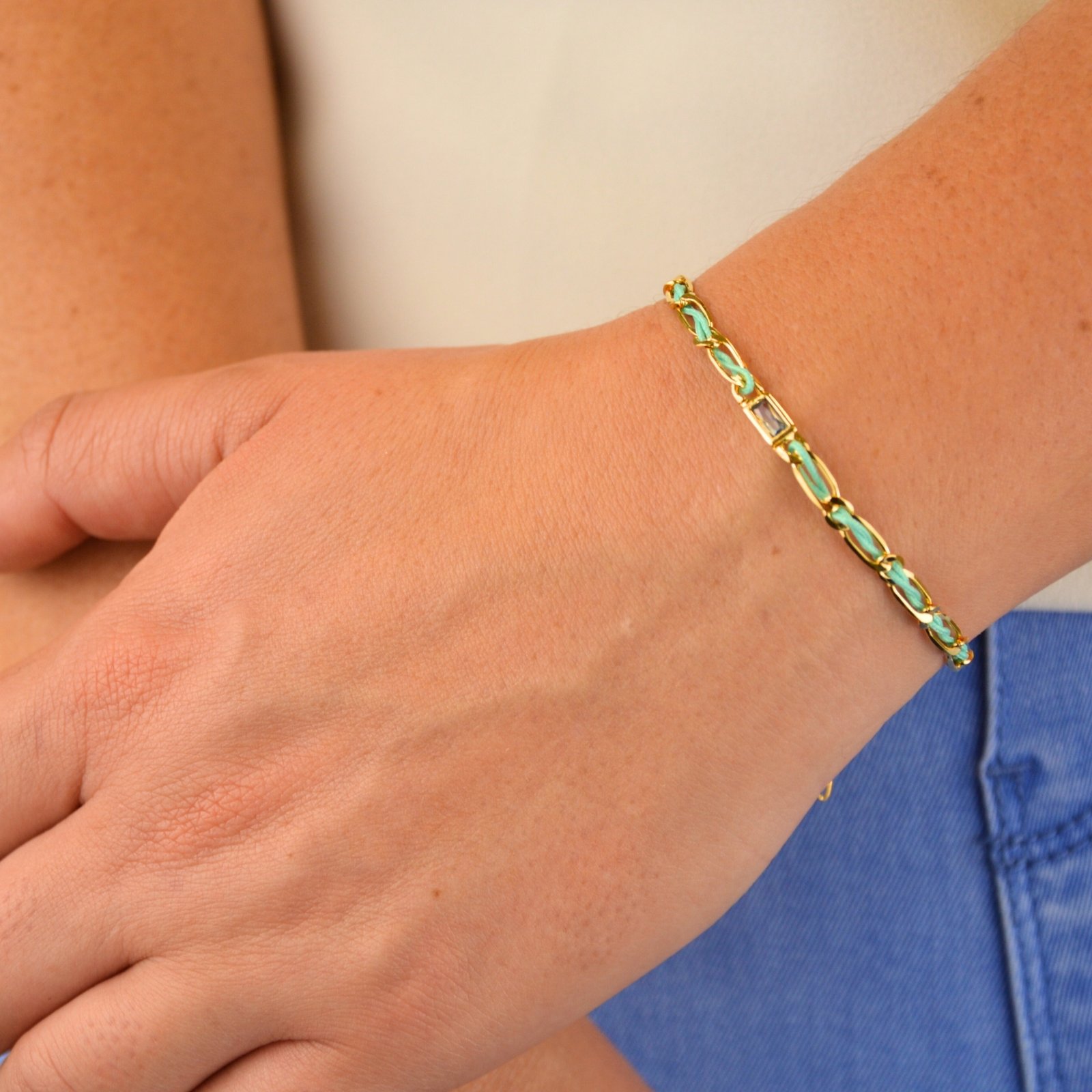 "Bracelet avec un cordon doré et un gemme transparent en son centre. Composition : 100% plaqué or. Contient 1 strass coloré transparent. . Bijou porté, Crédit GEMITY."