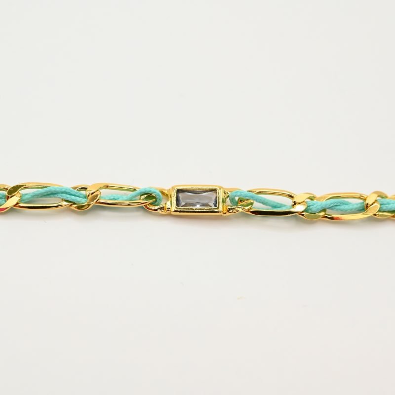 "Bracelet avec un cordon doré et un gemme transparent en son centre. Composition : 100% plaqué or. Contient 1 strass coloré transparent. . Bijou seul, Crédit GEMITY"
