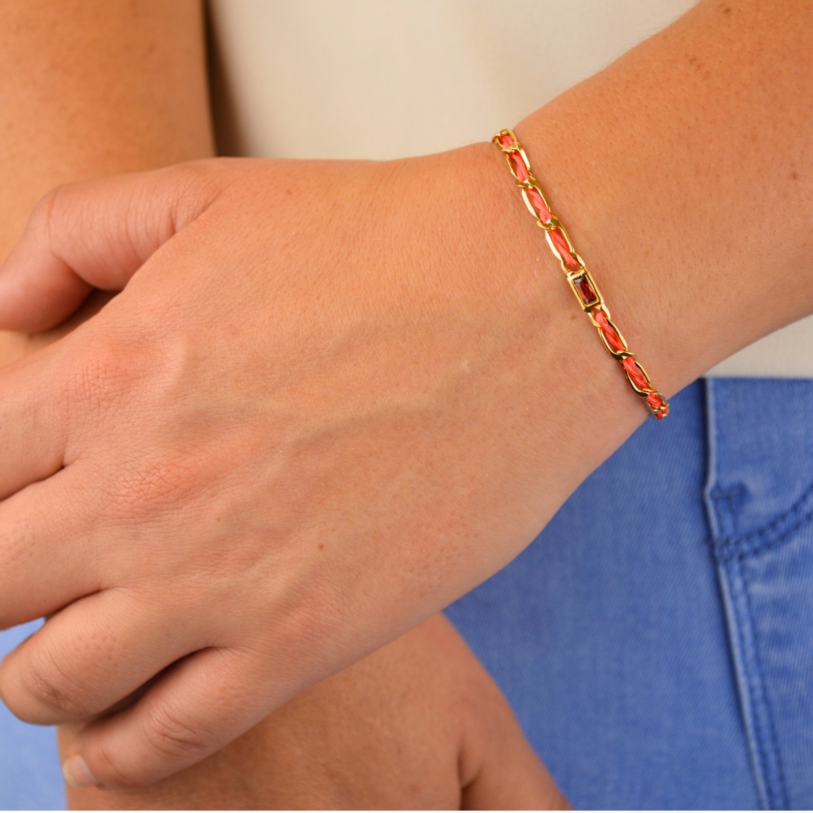 "Bracelet avec un cordon doré et un gemme transparent en son centre. Composition : 100% plaqué or. Contient 1 strass coloré transparent. . Bijou porté, Crédit GEMITY."