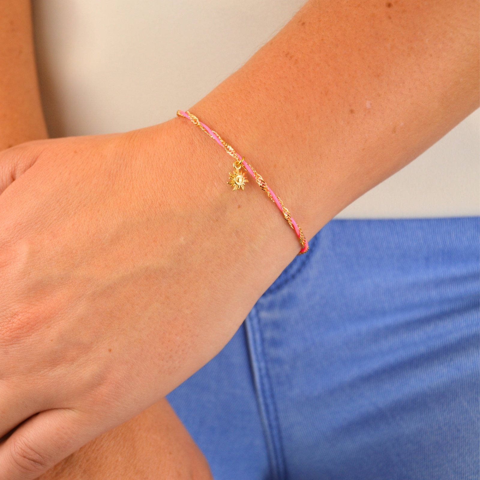 "L’élégance décontractée de la côte basque. Ce bracelet mêle fils de coton torsadé, touches dorées et couleurs vibrantes, pour une alliance parfaite entre raffinement et fraîcheur de l’océan. Orné d'un charm, il incarne une harmonie bohème et sophistiquée à porter au quotidien. Composition : Plaqué or et fils de coton torsadés. . Bijou porté, Crédit GEMITY."