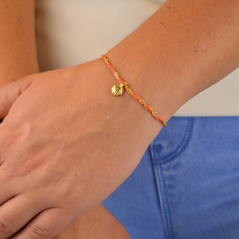 "L’élégance décontractée de la côte basque. Ce bracelet mêle fils de coton torsadé, touches dorées et couleurs vibrantes, pour une alliance parfaite entre raffinement et fraîcheur de l’océan. Orné d'un charm, il incarne une harmonie bohème et sophistiquée à porter au quotidien. Composition : Plaqué or et fils de coton torsadés. . Bijou porté, Crédit GEMITY."