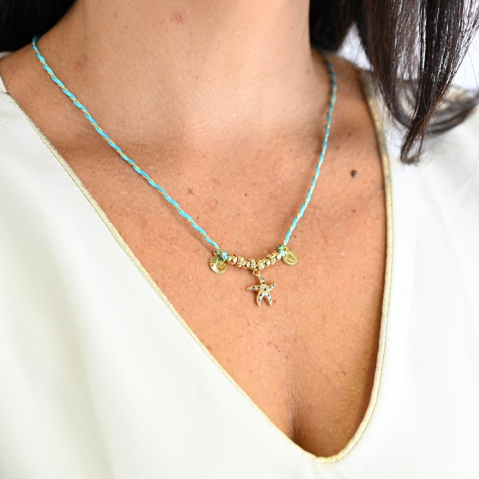 "L’élégance décontractée de la côte basque. Ce bracelet mêle fils de coton torsadé, touches dorées et couleurs vibrantes, pour une alliance parfaite entre raffinement et fraîcheur de l’océan. Orné d'un charm, il incarne une harmonie bohème et sophistiquée à porter au quotidien. Composition : Plaqué or et fils de coton torsadés. . Bijou porté, Crédit GEMITY."