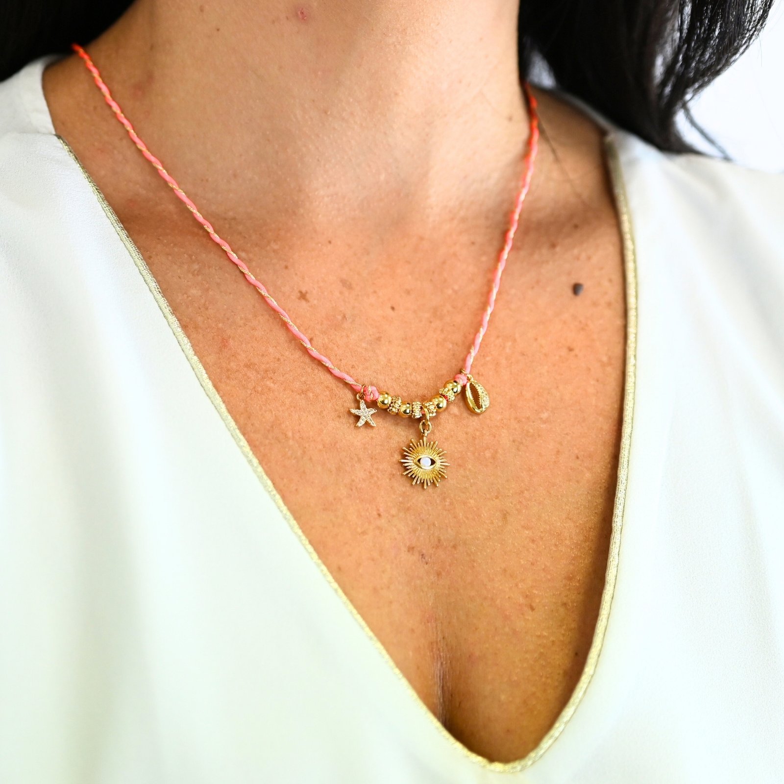 "Ces colliers mêlent fils de coton torsadé, touches dorées et couleurs vibrantes, pour une alliance parfaite entre raffinement et fraîcheur de l’océan. Ornés de trois charms et de détails en plaqué or, ils rappellent l’énergie chic des vagues et le charme intemporel des rivages de Biarritz. Une harmonie bohème et sophistiquée à porter au quotidien. Composition : Plaqué or et fils de coton torsadés. . Bijou porté, Crédit GEMITY."