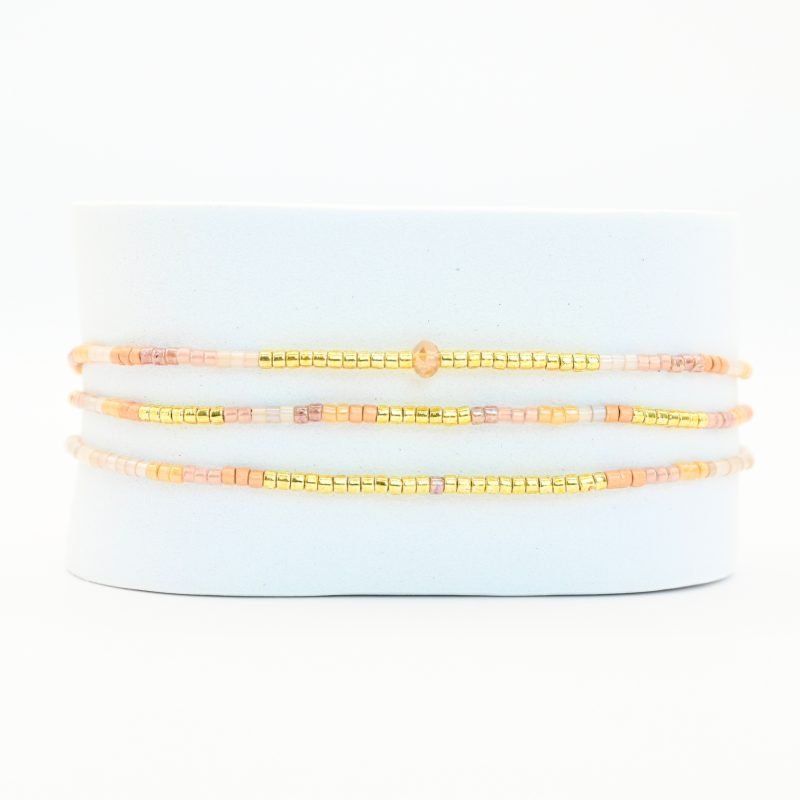 ce bracelet fin à 3 rangs combine des perles dorées, nude et dans les tons rosés pour un design doux et féminin. L'un des rangs est orné d'une plus grande perle au centre, apportant une touche de sophistication et de brillance. . Bijou seul, Crédit GEMITY