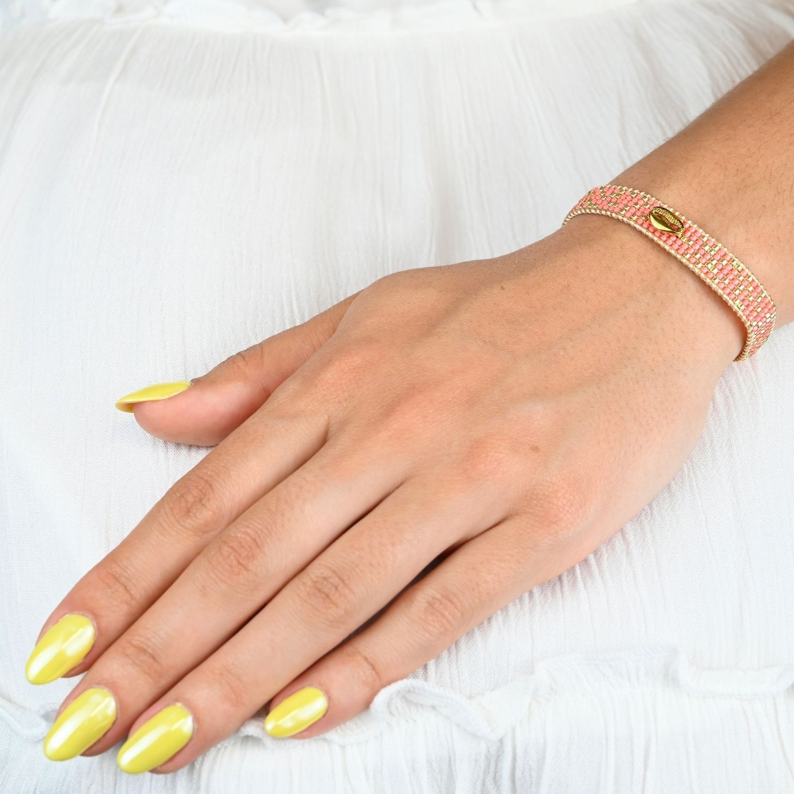 laissez-vous séduire par la beauté naturelle de cette petite manchette, composée de 5 rangs de perles corail soigneusement assemblées. L'ornement coquillage en son centre ajoute une touche marine et exotique, parfaite pour les amateurs de style bohème et élégant.. Bijou porté, Crédit GEMITY.