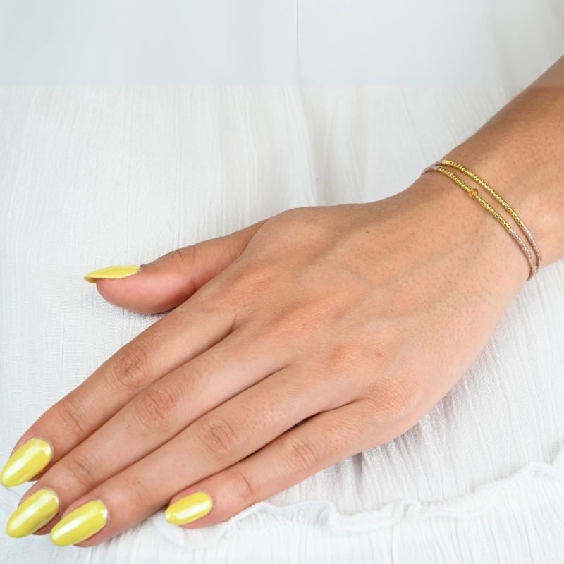 ce bracelet raffiné, composé de deux rangs, est l'accessoire parfait pour apporter de l'élégance à votre poignet. Le design associe des perles dorées et des perles nude, avec une disposition qui crée un équilibre parfait. . Bijou porté, Crédit GEMITY.