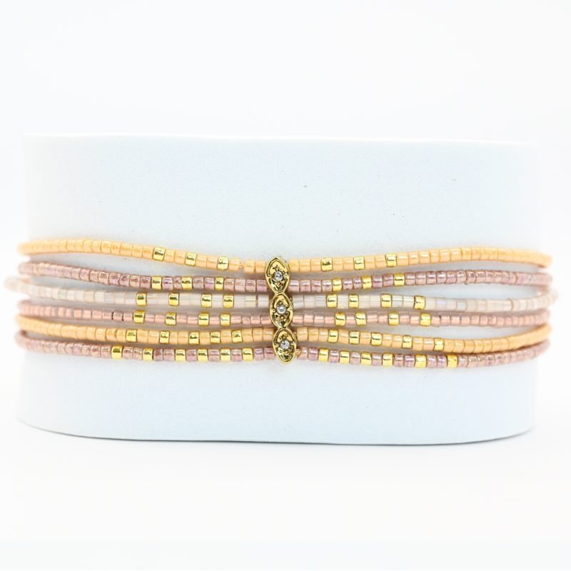 ce bracelet fin à 6 rangs associe des perles dorées et nude pour un look élégant et raffiné. Un ornement traverse les six rangs, créant un effet unique et structuré. . Bijou seul, Crédit GEMITY