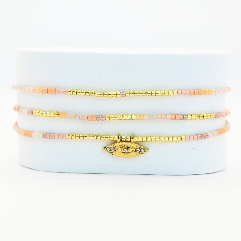 ce bracelet à 3 rangs combine des perles dorées, nude et rose poudré. Le second rang est orné d’un charm œil au centre, ajoutant une touche originale et élégante. . Bijou seul, Crédit GEMITY