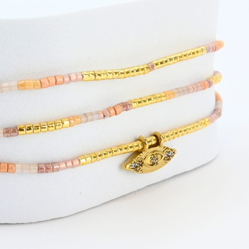 ce bracelet à 3 rangs combine des perles dorées, nude et rose poudré. Le second rang est orné d’un charm œil au centre, ajoutant une touche originale et élégante. . Bijou seul, Crédit GEMITY
