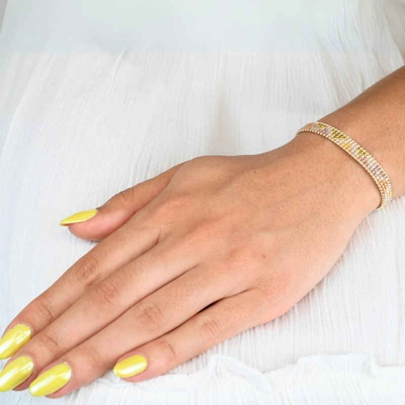 cette mini manchette élégante se compose de 3 rangs de perles nude, dorées et blanches, créant un design délicat et raffiné. . Bijou porté, Crédit GEMITY.
