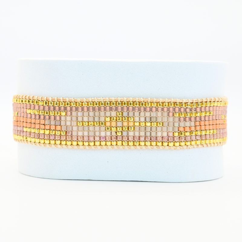 cette manchette élégante et sophistiquée se compose de 9 rangs de perles nude et dorées, créant un équilibre subtil entre douceur et éclat. Un motif central blanc apporte une touche lumineuse et raffinée. . Bijou seul, Crédit GEMITY