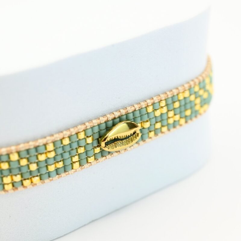 apportez une touche marine et raffinée à votre poignet avec cette petite manchette composée de 5 rangs de perles dorées et vert d'eau. L'ornement coquillage en son centre évoque l'univers maritime, apportant une note délicate et exotique à ce bijou.. Bijou seul, Crédit GEMITY
