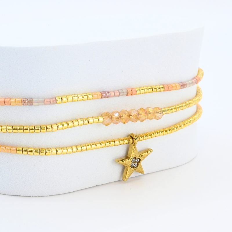 ce bracelet raffiné à 3 rangs combine des perles dorées et nude pour un look élégant et féminin. Le premier rang est orné de perles délicates, tandis que le second présente des perles plus grosses, créant un effet visuel dynamique. Le troisième rang se distingue par un charm étoile au centre, ajoutant une touche de magie et de sophistication. . Bijou seul, Crédit GEMITY