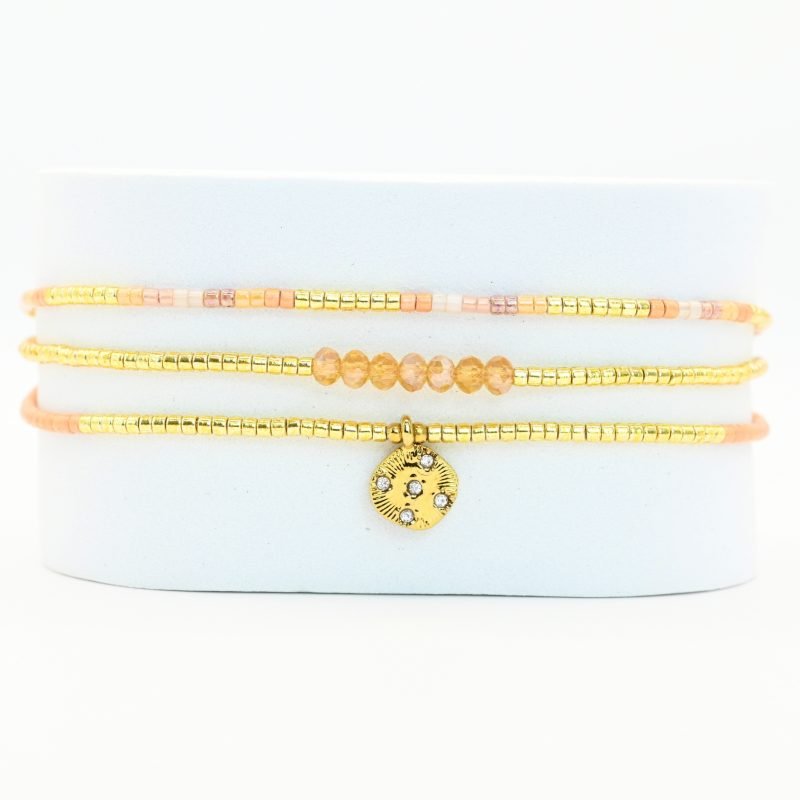 ce bracelet fin à 3 rangs combine des perles dorées, nude et roses, créant une harmonie de couleurs douce et élégante. Le charm rond à strass, placé au centre, ajoute une touche scintillante et raffinée. . Bijou seul, Crédit GEMITY
