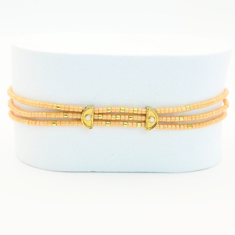 ce bracelet fin à 3 rangs est principalement composé de perles nude, avec quelques touches subtiles de perles dorées, créant un look délicat et élégant. Les trois rangs sont réunis par deux ornements en forme de lune, apportant une touche mystique et raffinée. . Bijou seul, Crédit GEMITY