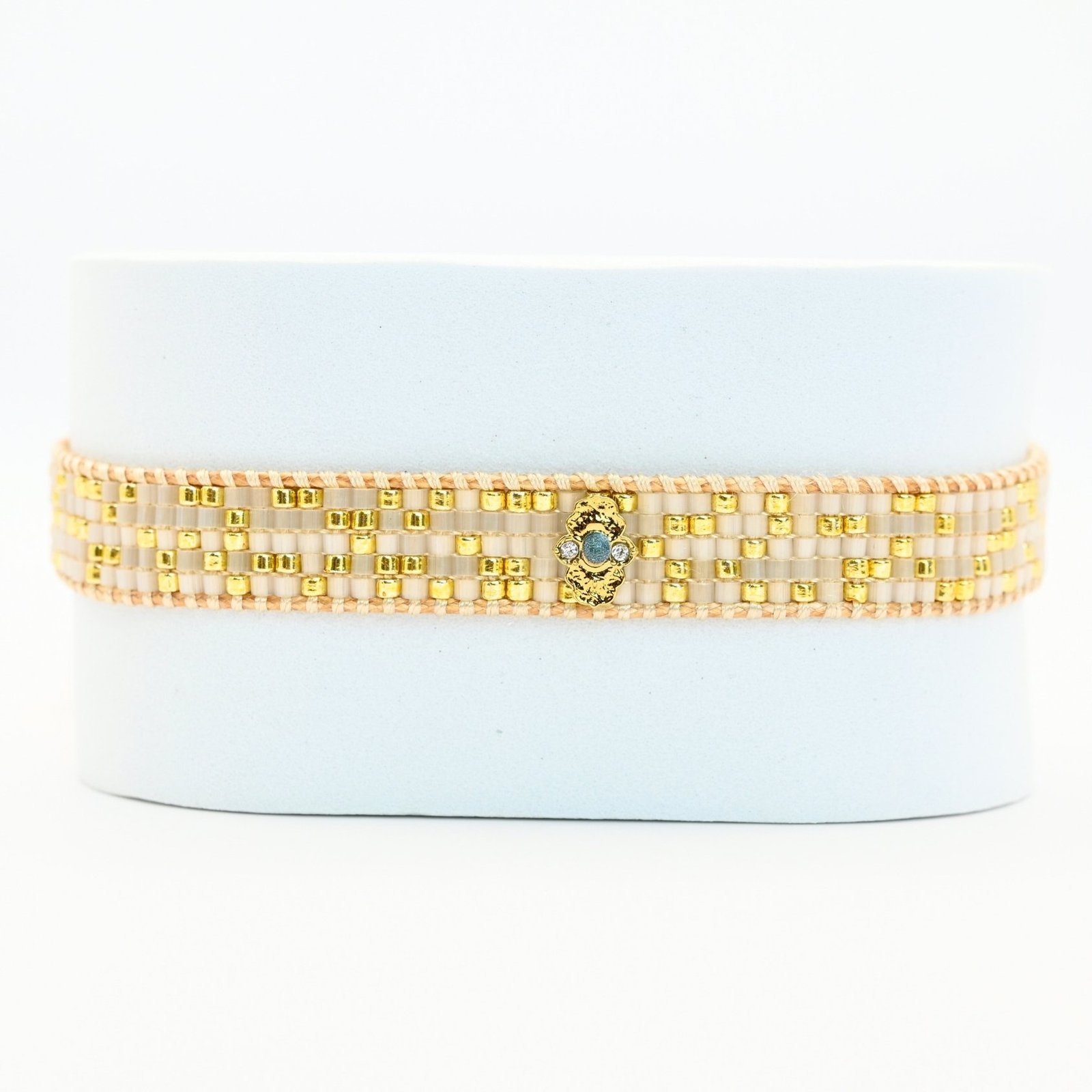 ajoutez une touche de sophistication à votre poignet avec cette petite manchette composée de 5 rangs de perles dorées et blanches. L'ornement doré en son centre apporte une touche de brillance et d'élégance supplémentaire à ce bijou délicat.. Bijou seul