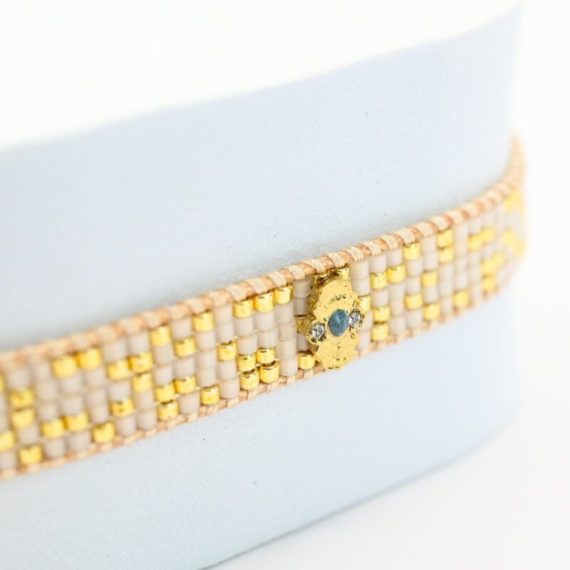 ajoutez une touche de sophistication à votre poignet avec cette petite manchette composée de 5 rangs de perles dorées et blanches. L'ornement doré en son centre apporte une touche de brillance et d'élégance supplémentaire à ce bijou délicat.. Bijou seul, Crédit GEMITY