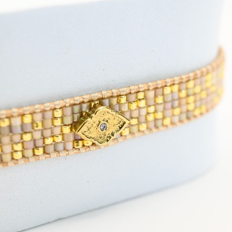cette petite manchette délicate associe 5 rangs de perles nude et dorées pour un effet élégant et raffiné. En son centre, un ornement inspiré des motifs orientaux ajoute une touche de mystère et d'exotisme. . Bijou seul, Crédit GEMITY