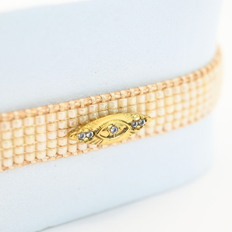 cette petite manchette raffinée se compose de 5 rangs de perles blanches, offrant une touche lumineuse et élégante. Son ornement central en forme d'œil apporte une symbolique protectrice et tendance. . Bijou seul, Crédit GEMITY
