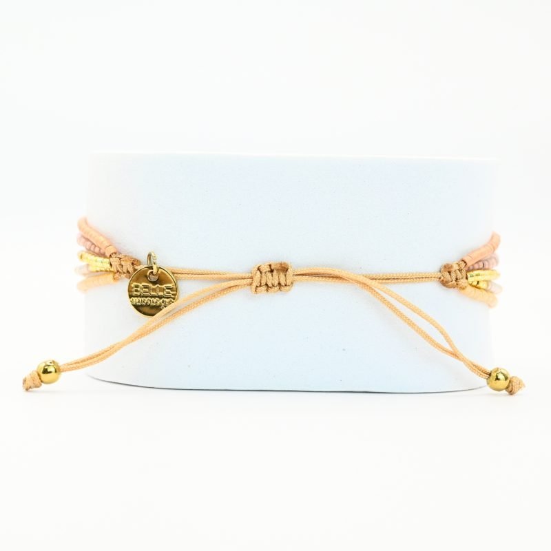 ce bracelet fin à 5 rangs combine des perles dorées, nude, blanches et dans les tons rosés, créant un design doux et harmonieux. Un charm fleur doré, avec un zircon au centre, est placé sur un fond blanc en forme ovale sur l’un des rangs, ajoutant une touche élégante et raffinée. . Bijou seul, Crédit GEMITY