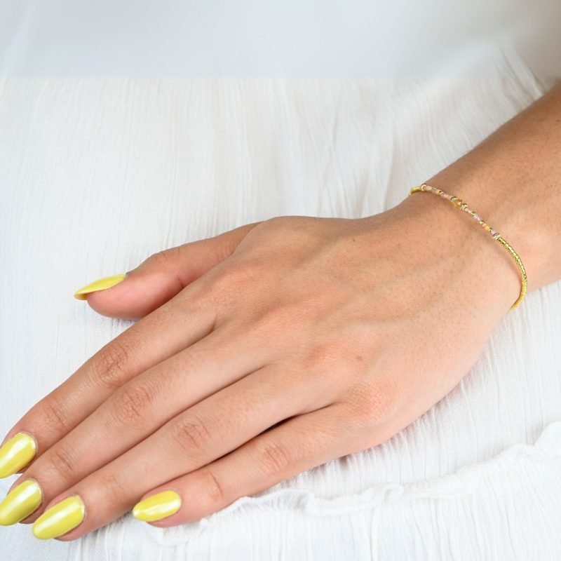 ce bracelet fin et délicat joue sur l’harmonie des couleurs avec son cordon ajustable, ses perles dorées et ses perles dans les tons roses placées en son centre. . Bijou porté, Crédit GEMITY.