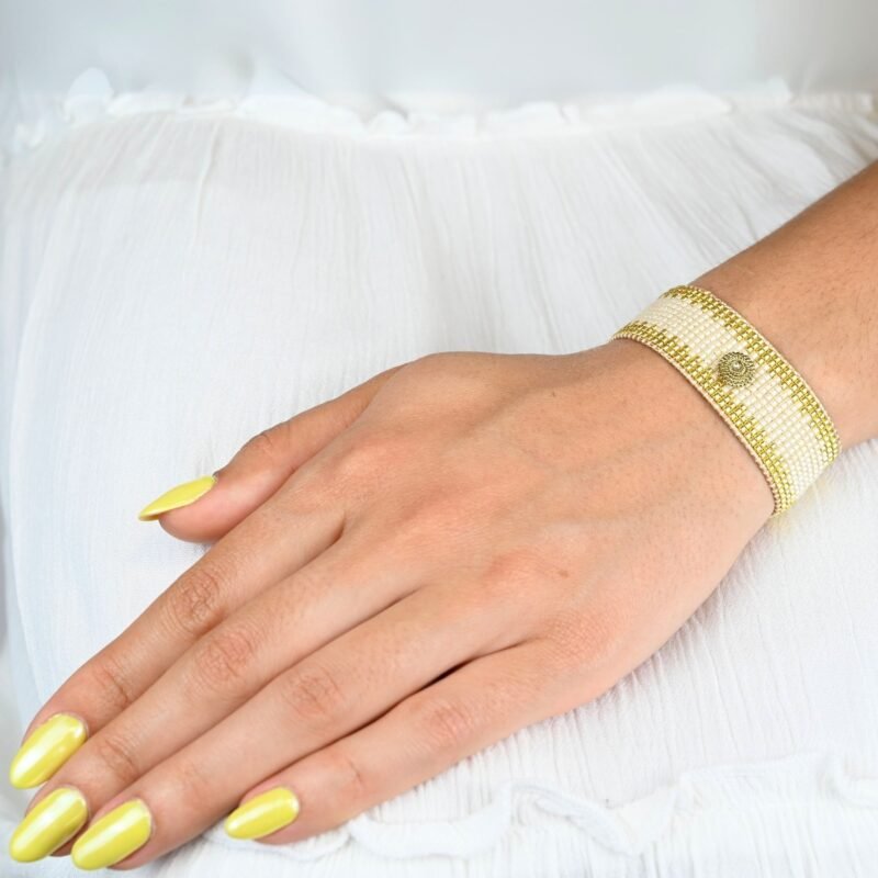 cette grande manchette élégante se compose de 12 rangs de perles dorées et nude, offrant un mélange subtil de luminosité et de douceur. L'ornement cercle au centre ajoute une touche contemporaine et raffinée, créant un look moderne et intemporel.. Bijou porté, Crédit GEMITY.