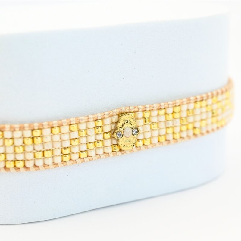 cette petite manchette délicate se compose de 5 rangs de perles nude et dorées, apportant une touche douce et lumineuse à votre poignet. Son ornement central en forme de lotus doré symbolise l’harmonie et la sérénité. . Bijou seul, Crédit GEMITY