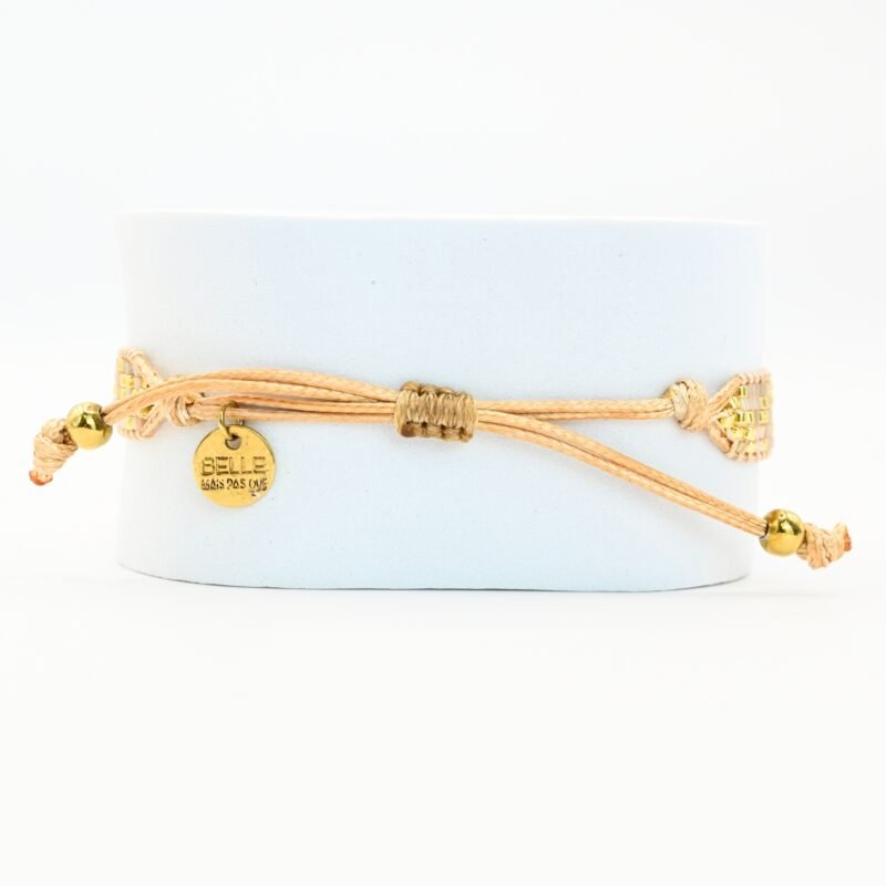 cette petite manchette délicate se compose de 5 rangs de perles nude et dorées, apportant une touche douce et lumineuse à votre poignet. Son ornement central en forme de lotus doré symbolise l’harmonie et la sérénité. . Bijou seul, Crédit GEMITY