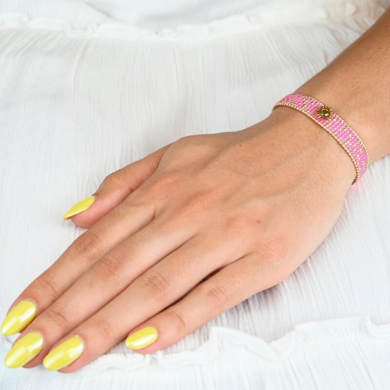 audacieuse et éclatante, cette petite manchette illumine votre poignet avec ses 5 rangs de perles roses fluo. Son ornement central en forme de soleil apporte une touche lumineuse et rayonnante. . Bijou porté, Crédit GEMITY.