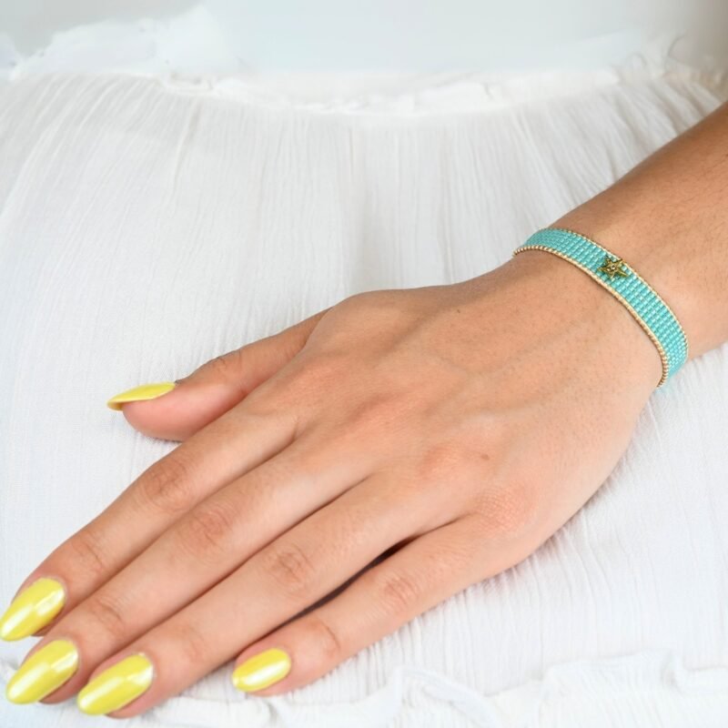 inspirée des nuances apaisantes de l’océan, cette petite manchette se compose de 5 rangs de perles bleues lagon. Son ornement étoile avec un zircon disposé au centre du bracelet apporte une touche lumineuse. . Bijou porté, Crédit GEMITY.