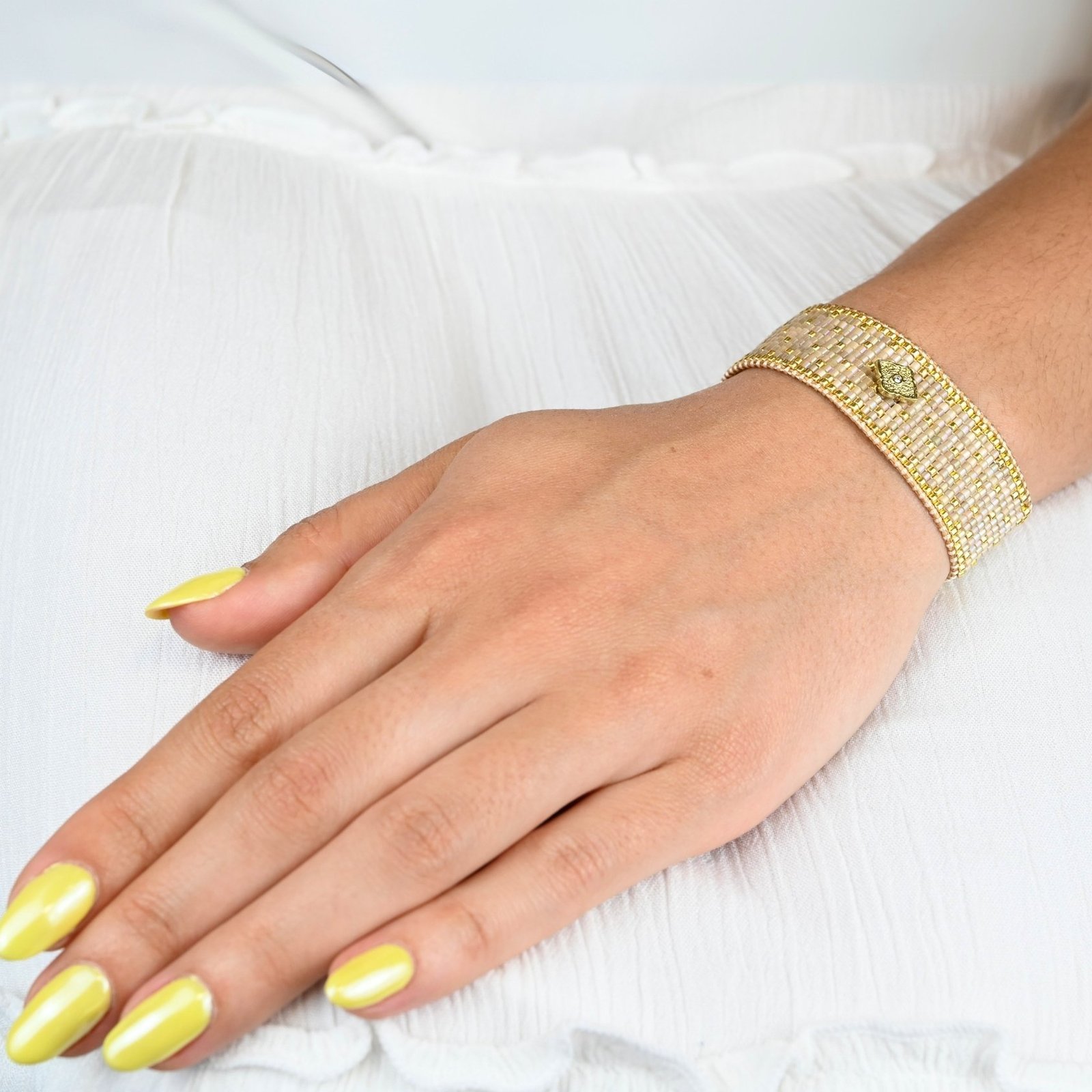 élégante et raffinée, cette grande manchette se compose de 12 rangs de perles dorées et nude, créant une texture luxueuse et un contraste subtil. L'ornement losange au centre ajoute une touche géométrique et moderne, apportant une touche d'originalité et de sophistication à ce bijou.. Bijou porté, Crédit GEMITY.