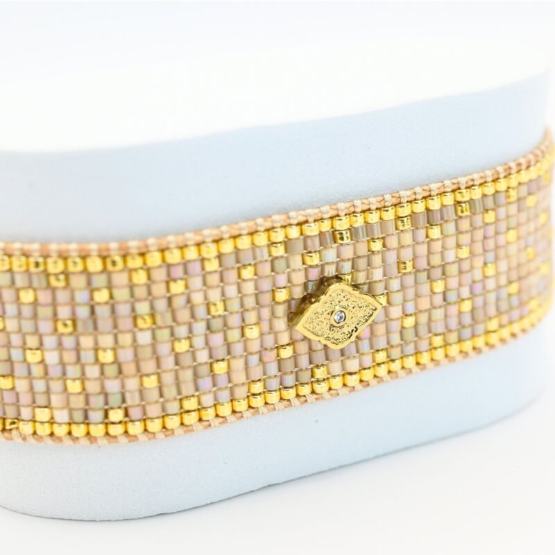 élégante et raffinée, cette grande manchette se compose de 12 rangs de perles dorées et nude, créant une texture luxueuse et un contraste subtil. L'ornement losange au centre ajoute une touche géométrique et moderne, apportant une touche d'originalité et de sophistication à ce bijou.. Bijou seul, Crédit GEMITY